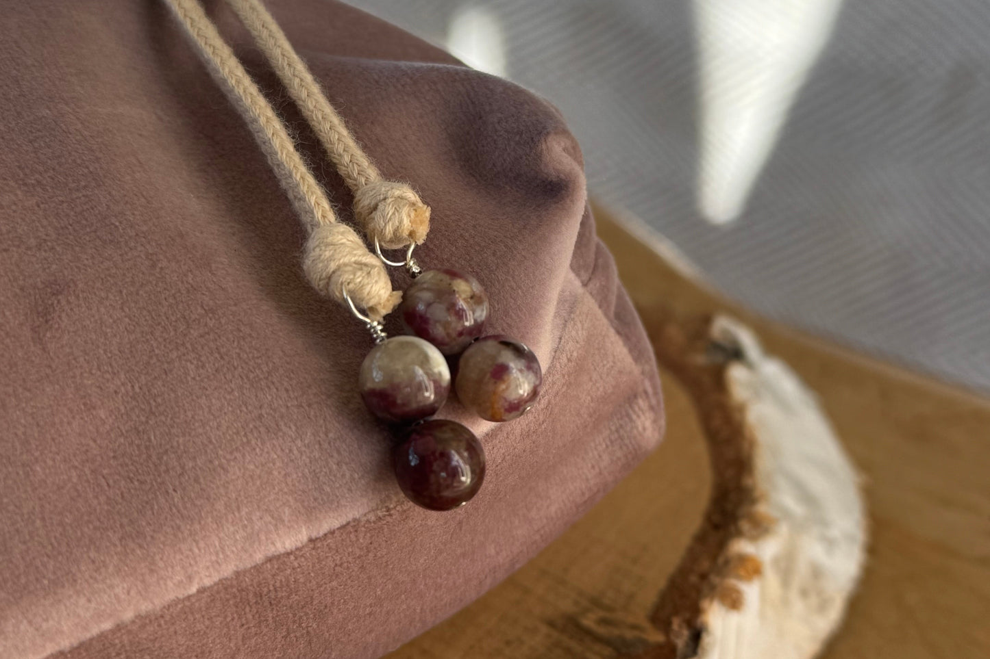 Close up of cherry tourmaline beads and cream cotton drawstring on a blush pink velvet background